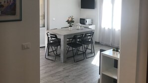 A modern, well-lit room with a dining table and chairs, a flat-screen TV mounted on the wall, and a small potted plant on the table. - Sant'antonino Apartments - Maestrale (levanto)