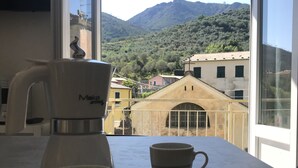 A table with a coffee maker and a cup, overlooking a mountainous landscape with buildings. - Sant'antonino Apartments - Maestrale (levanto)