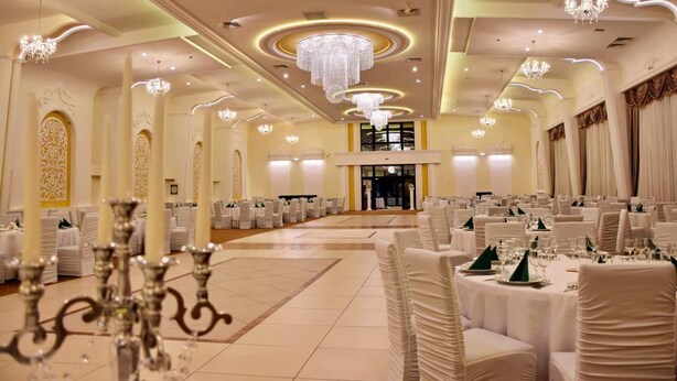 A banquet hall with round tables, chandeliers, and ornate wall decorations. - Hotel Polaris (Scheia)