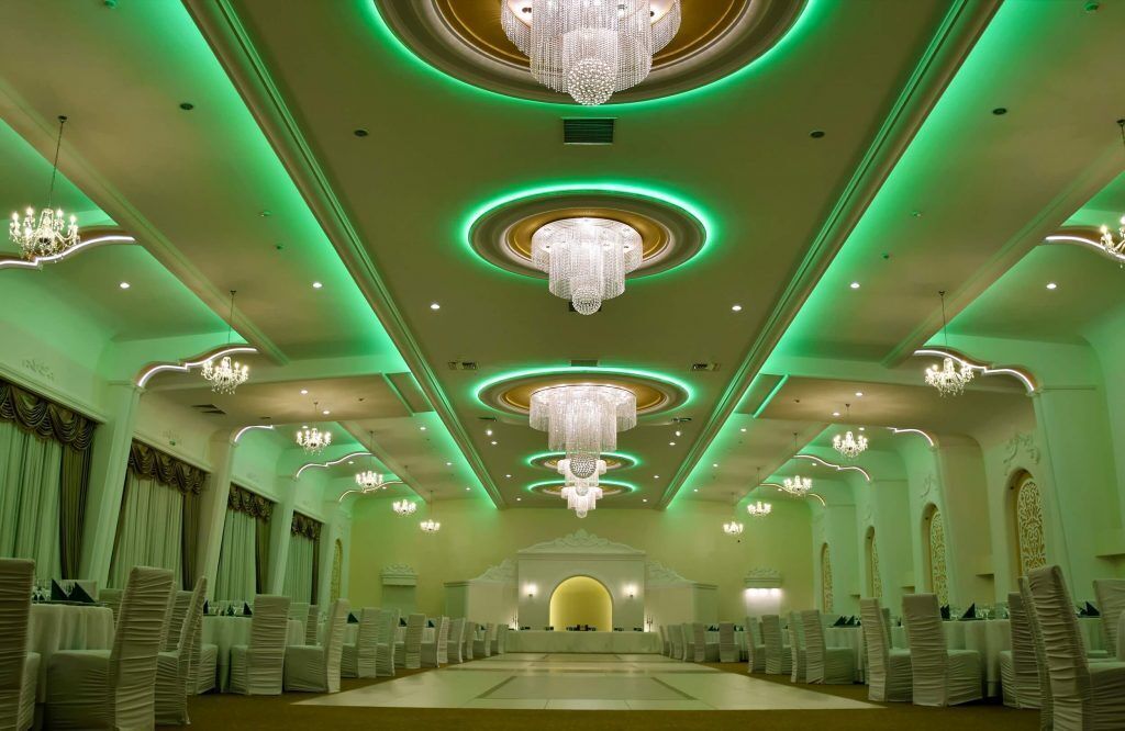 A banquet hall with tiered seating, chandeliers, and green ambient lighting.