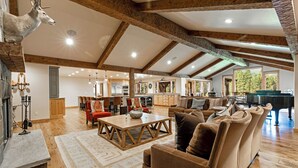 A spacious living area with a fireplace, wooden beams, a dining table, and a grand piano.