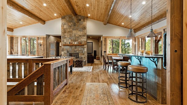 A spacious kitchen with a stone fireplace, wooden ceiling beams, and a bar area with stools.