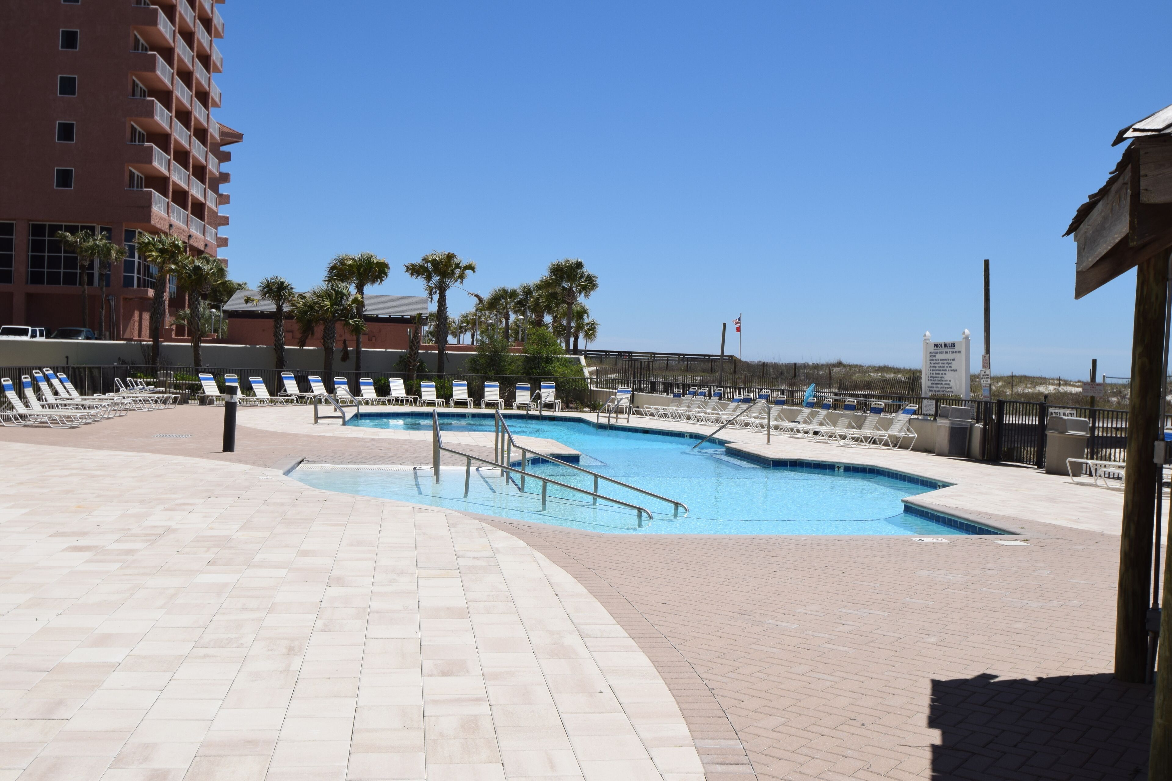 A swimming pool area with multiple pools, lounge chairs, and palm trees.