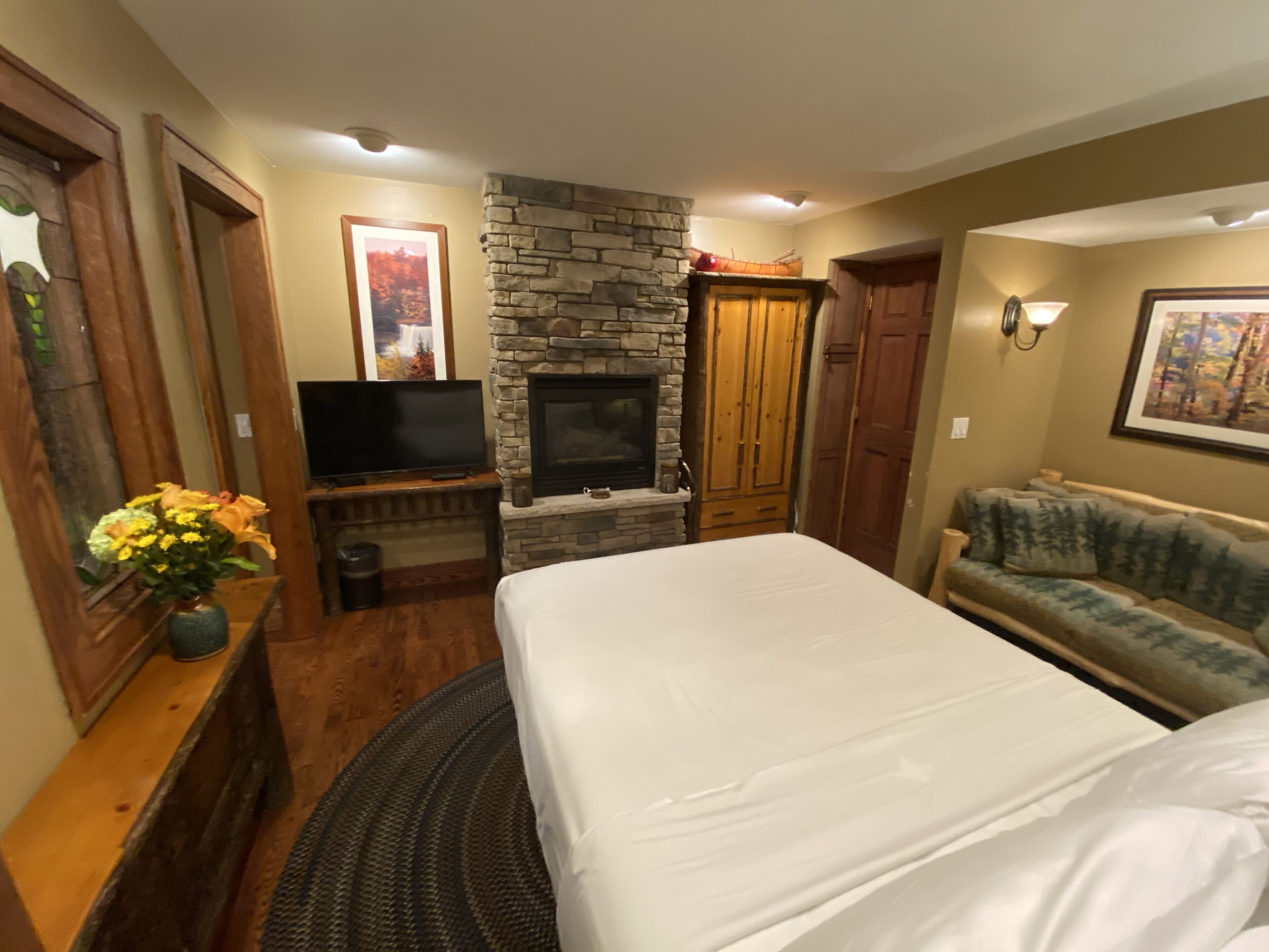 A bedroom with a bed, a television, a stone fireplace, a wooden wardrobe, and a couch.