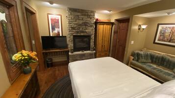A bedroom with a bed, a television, a stone fireplace, a wooden wardrobe, and a couch.