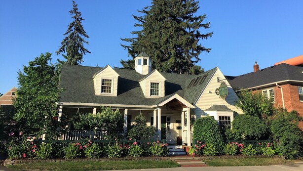 A two-story house with a gabled roof, a small tower-like structure on the roof, and a front porch. - Wild Goose Inn (East Lansing)