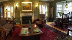 A cozy living room with a fireplace, patterned furniture, and a dining area with chairs and a table. - Wild Goose Inn (East Lansing)