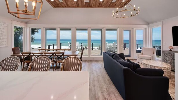 A spacious living area with a large window overlooking the beach, wooden ceiling, and modern furniture.