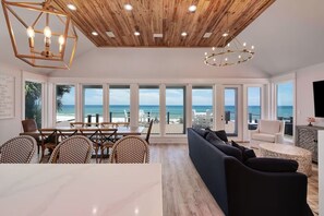 Ein großzügiger Wohnbereich mit großem Fenster zum Strand, Holzboden und modernen Möbeln.