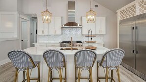 A modern kitchen with white cabinetry, a central island with bar stools, a stainless steel refrigerator, and pendant lighting.