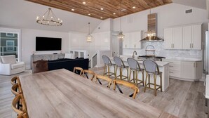 A modern kitchen with white cabinets, a wooden ceiling, and pendant lighting.