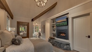 Une chambre à coucher avec un lit, une cheminée, un téléviseur fixé au-dessus de la cheminée et une porte donnant sur une autre pièce.
