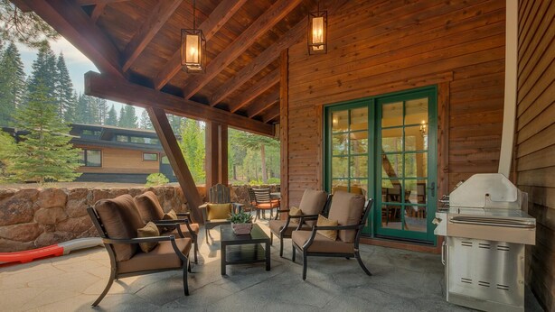 Une terrasse extérieure avec des meubles en bois, un barbecue et un mur en pierre.