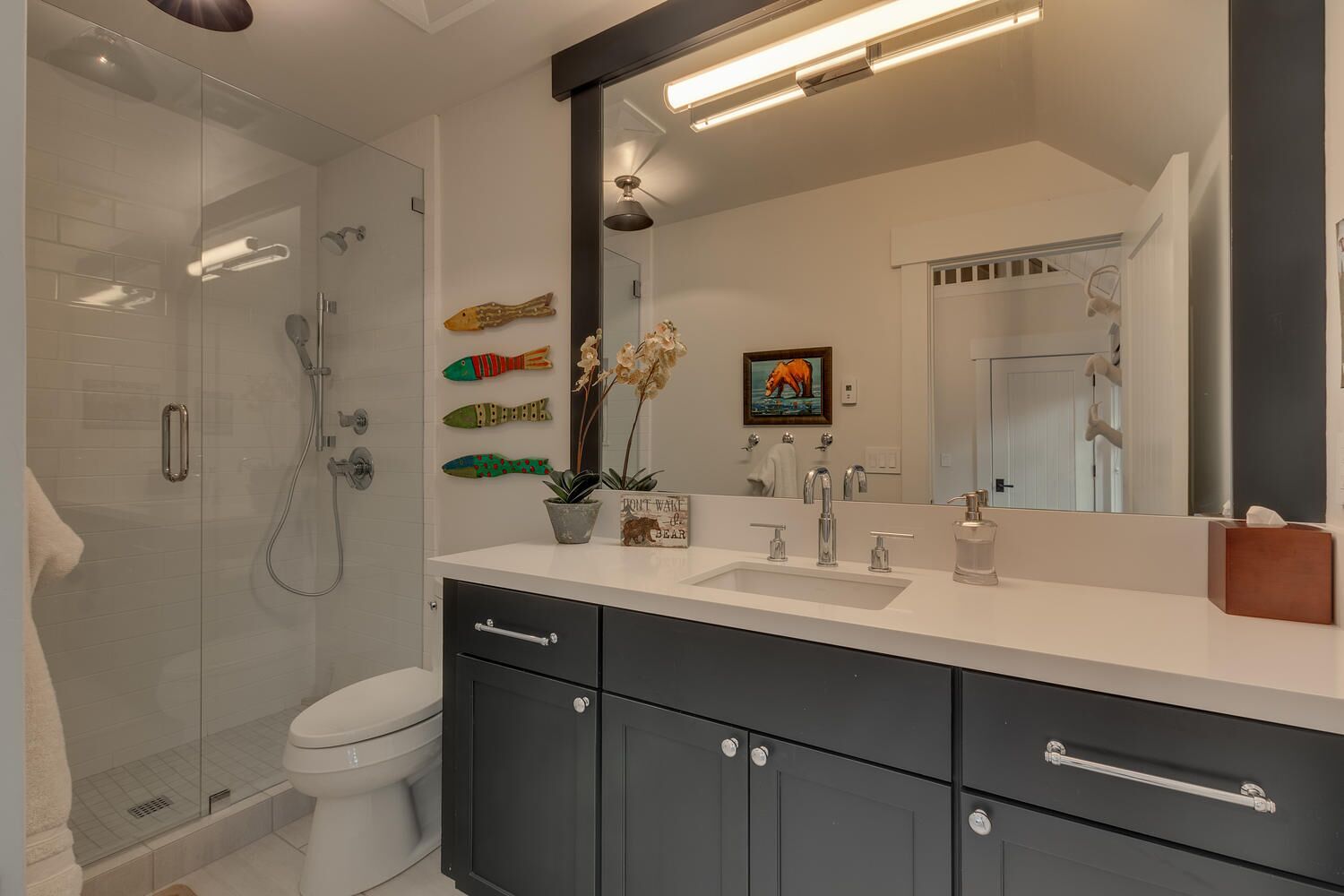 Un baño moderno con ducha de vidrio, inodoro blanco y tocador con un espejo grande.