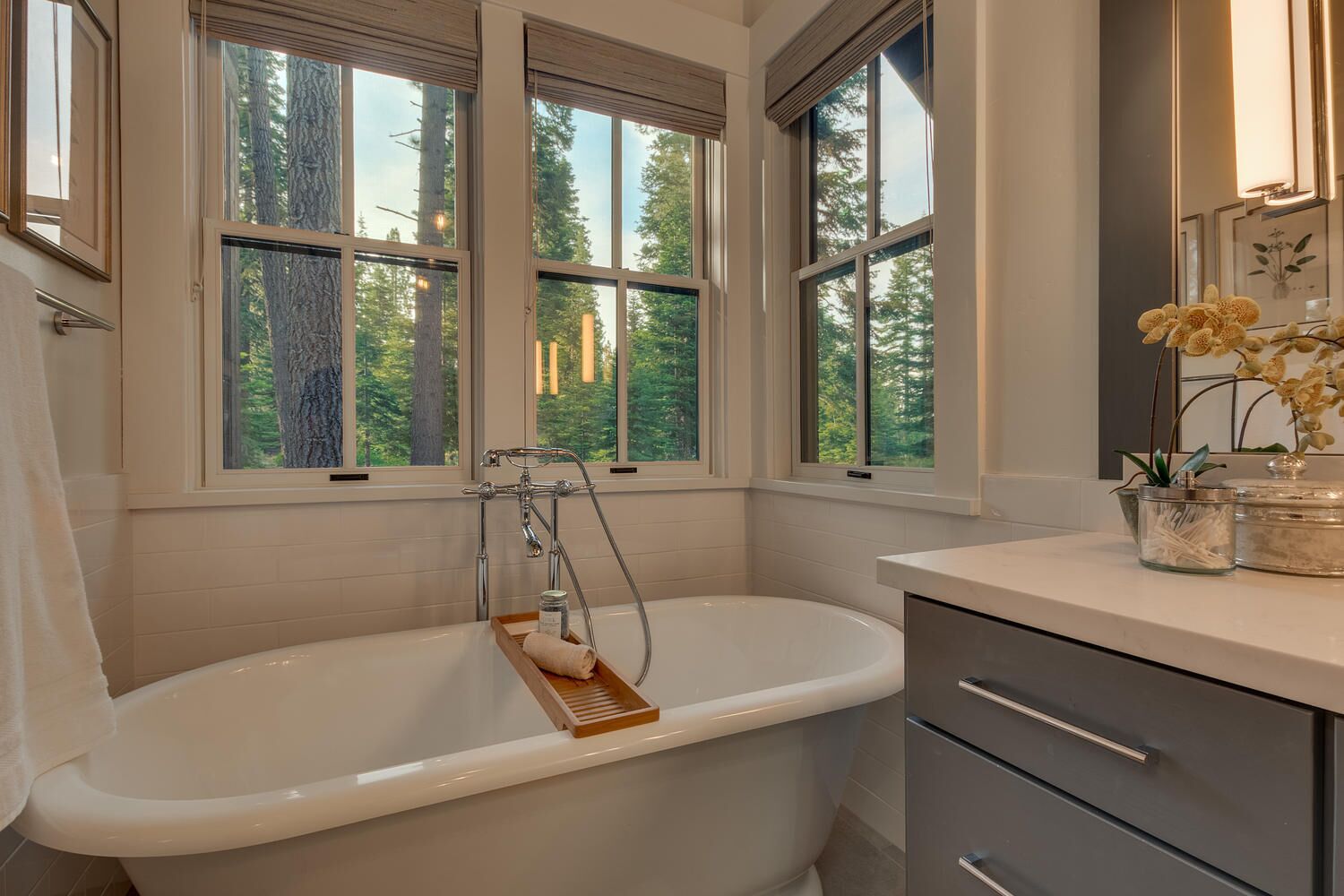 Une salle de bain avec une baignoire sur pieds, une fenêtre donnant sur la verdure et un meuble-lavabo agrémenté d’un miroir et d’une plante.