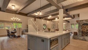 Une cuisine spacieuse dotée d’un grand îlot central, de poutres en bois et d’une cheminée en pierre.
