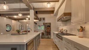 Une cuisine moderne dotée d’un grand îlot central, de poutres en bois et d’une cheminée en pierre.
