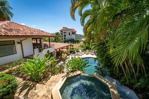 A pool area with a hot tub, surrounded by lush greenery and a building with a tiled roof. - Stunning Home with Brand-New Guesthouse and Oceanview Terrace with Private Swimming Pool & Hot Tub (Playa Flamingo)