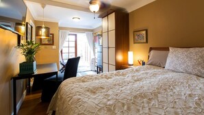 A hotel room with a large bed, a desk with a chair, a potted plant, and a ceiling fan. - Mar Vista Suite of Private Entry,Patio & Spa Bath (LOS ANGELES)