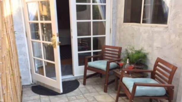 An outdoor patio area with two wooden chairs and a small table, a door leading to the interior, and a potted plant. - Mar Vista Suite of Private Entry,Patio & Spa Bath (LOS ANGELES)