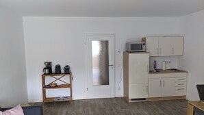 A compact living space with a kitchenette, a sofa with a cushion, and a wooden shelf with kitchen appliances. - Vacations in the historic city center of Zittau - IO19 / 2R (Zittau)
