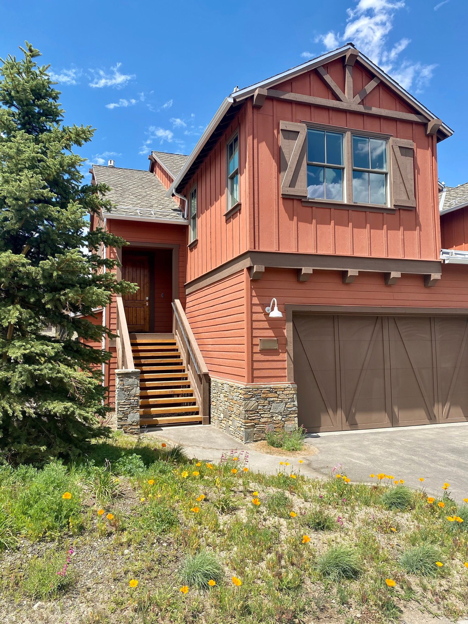 A two-story house with a red exterior, a stone foundation, and a wooden staircase leading to the front door.