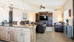 A spacious living room with a large TV, leather sofas, a dining area with a glass-top table, and wooden cabinets. - Canthony's Cottage - PICKLEBALL, Community Pool! Close to trails! (St George)