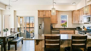 A modern kitchen with wooden cabinets, stainless steel appliances, and a large island with bar stools. - Canthony's Cottage - PICKLEBALL, Community Pool! Close to trails! (St George)
