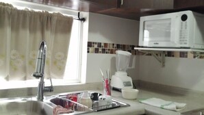 Una cocina con armarios de madera oscura, un lavamanos de acero inoxidable, un microondas blanco y una licuadora sobre la encimera.