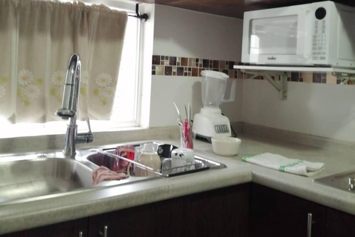 A kitchen with dark wooden cabinets, a stainless steel sink, a white microwave, and a blender on the countertop.