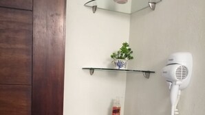 Un baño con puerta de madera, cabina de ducha de vidrio y secador de pelo blanco fijado a la pared.