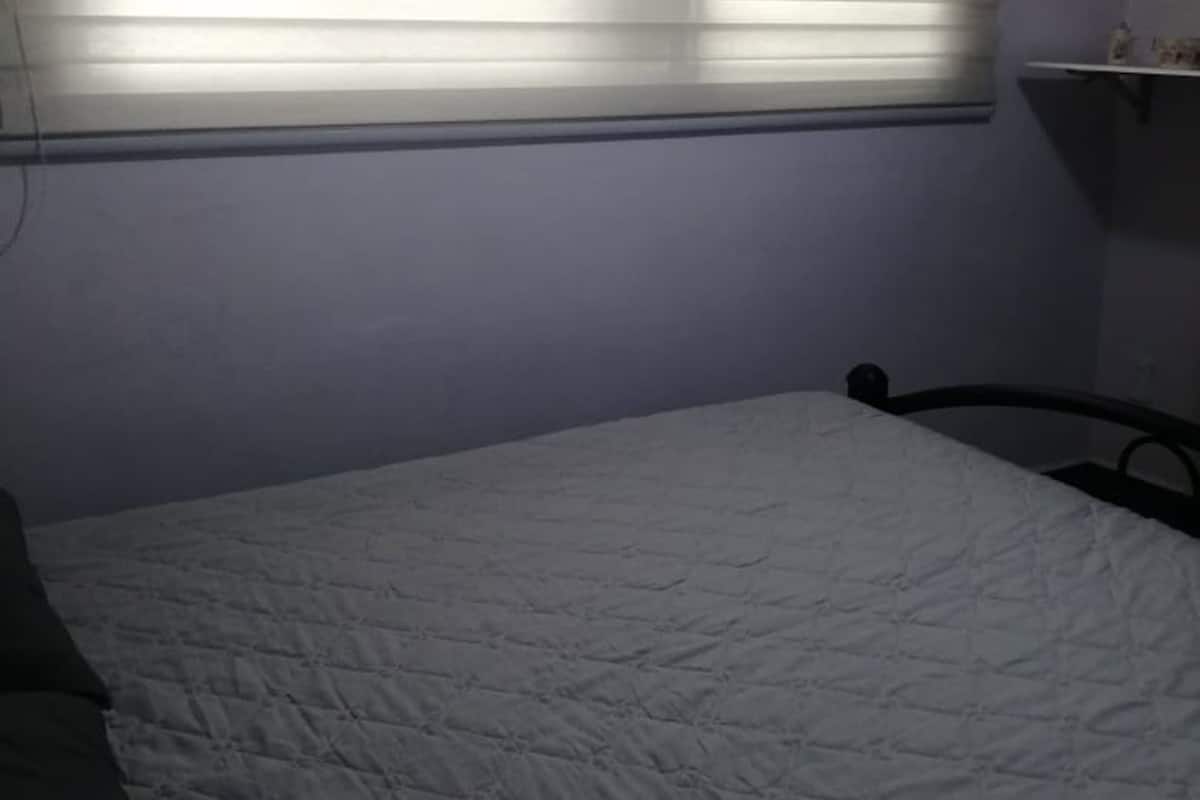 A bedroom with a bed, a window with blinds, and a shelf with items.