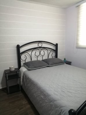 A bedroom with a bed, a nightstand, and a small table with a plant.