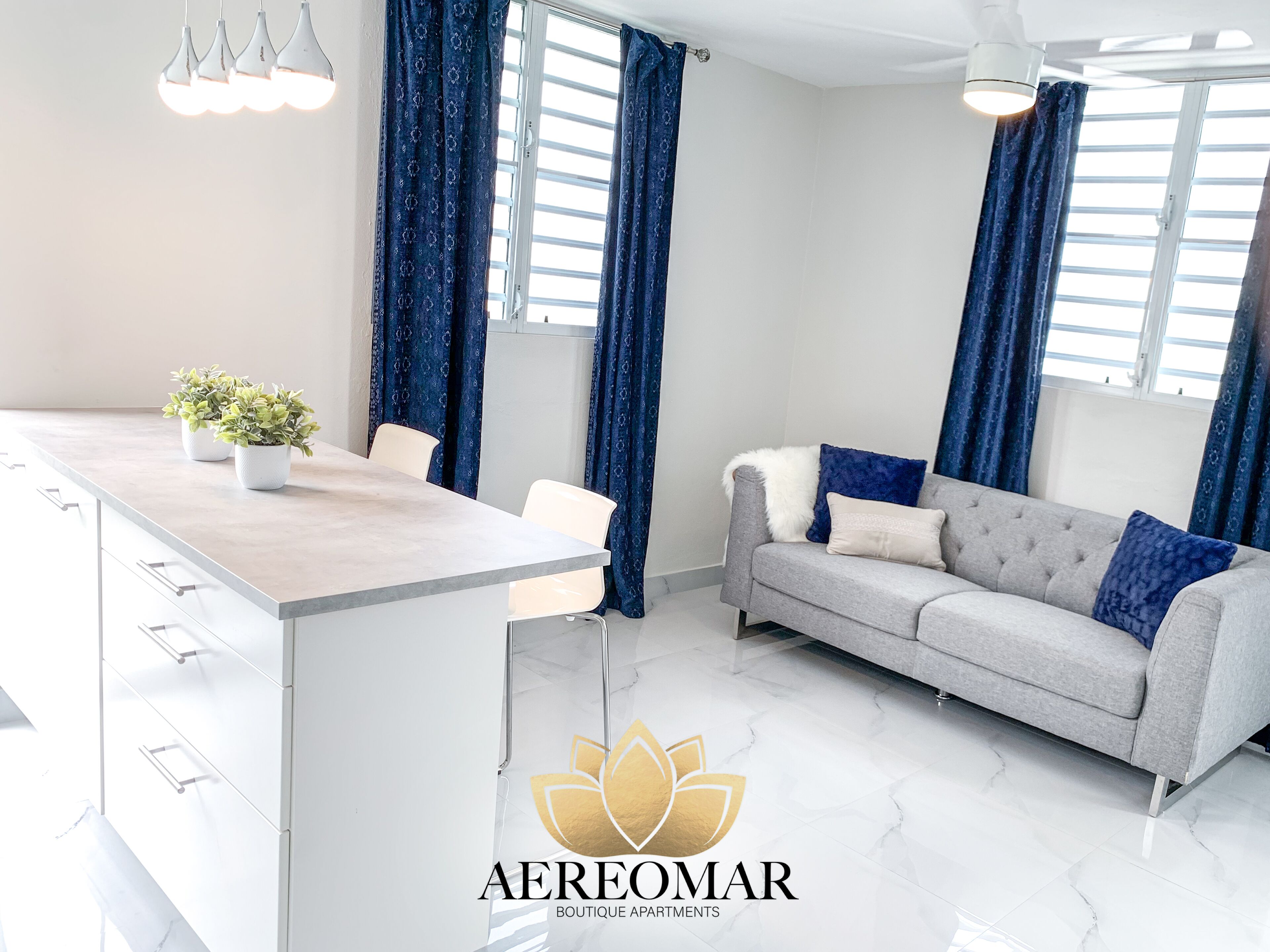 A modern living room with a grey sofa, a white coffee table, and blue patterned curtains.