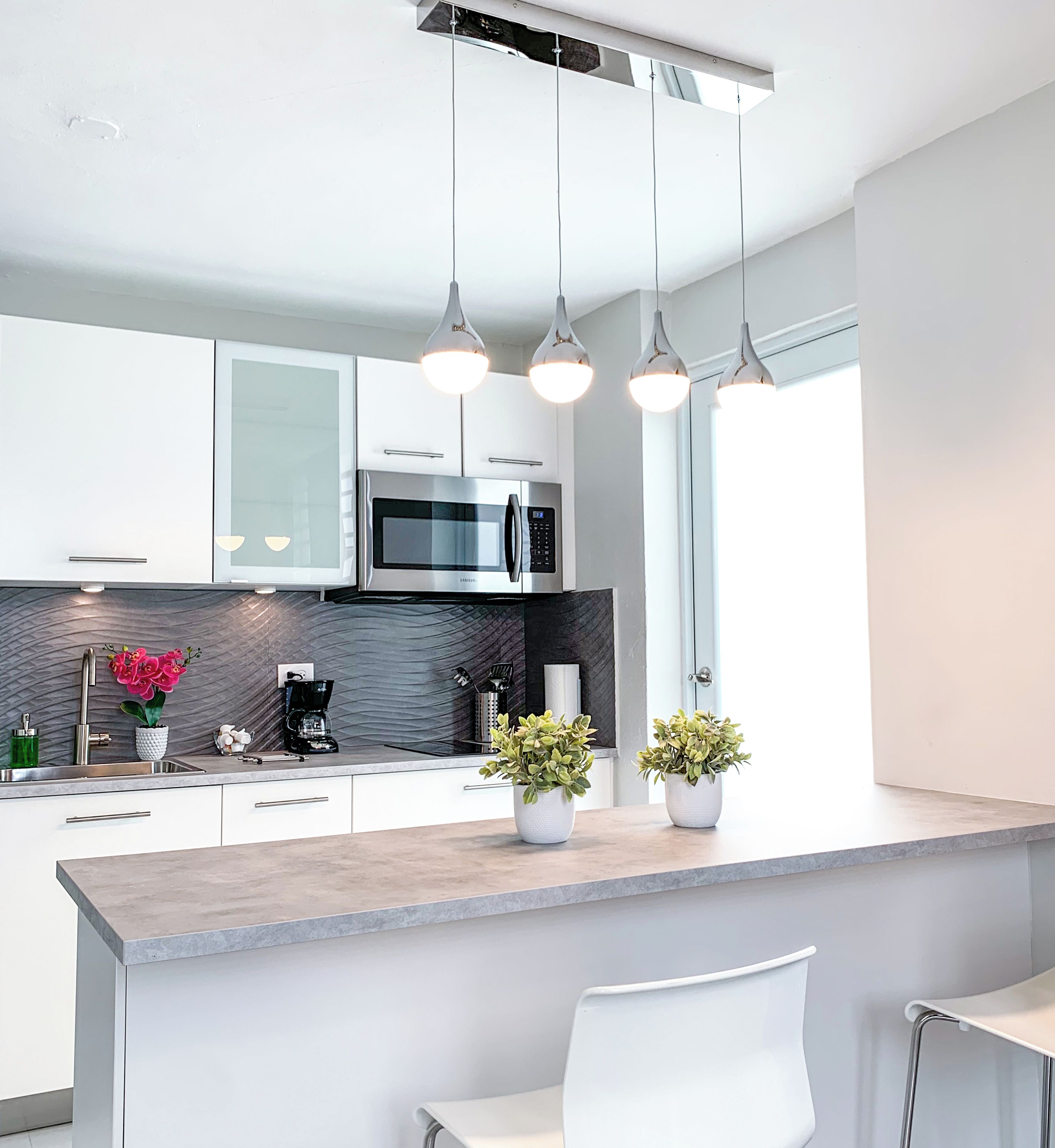 A modern kitchen with white cabinets, a built-in microwave, and pendant lighting.