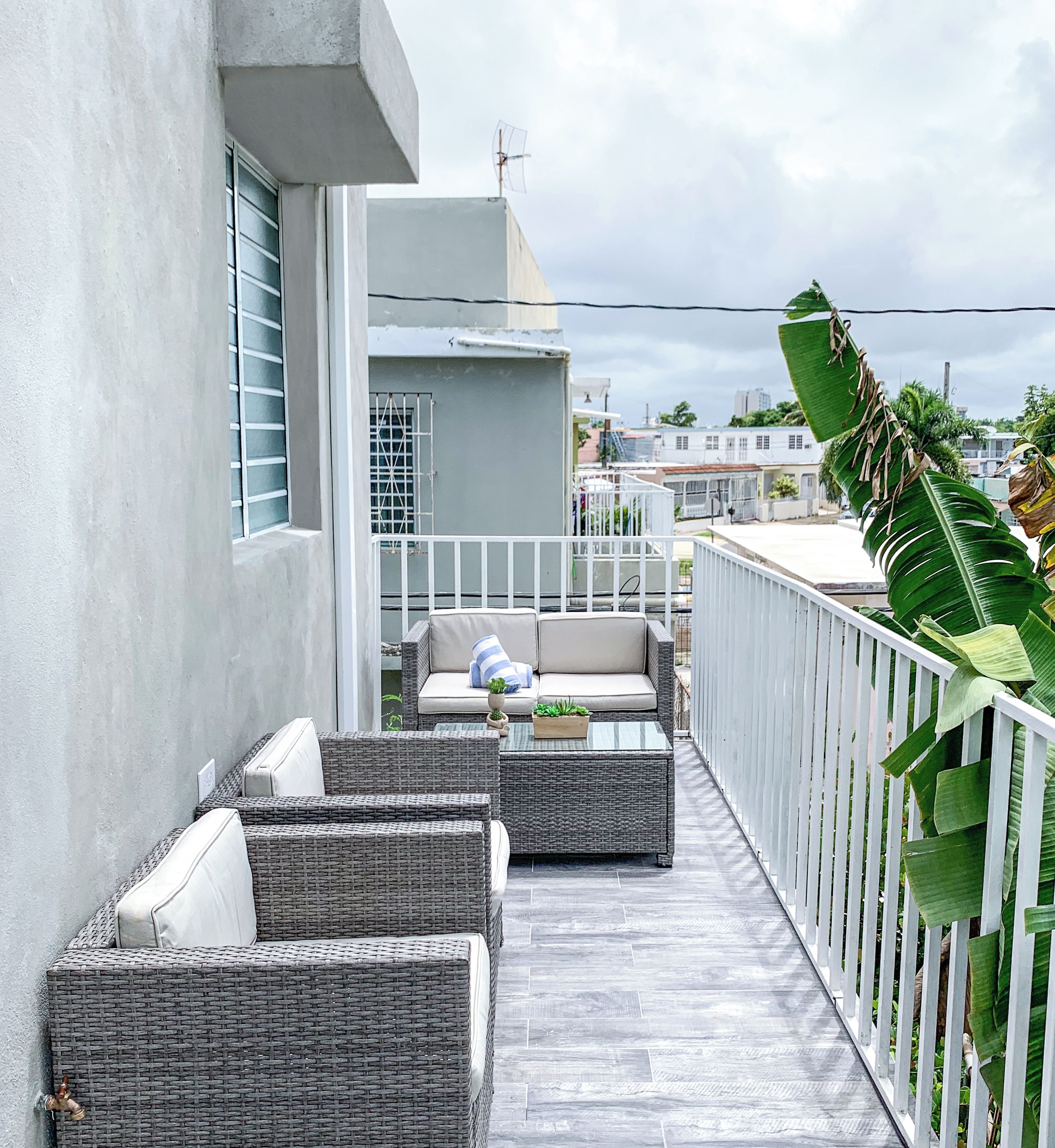 A balcony with wicker furniture, a small table with a plant, and a white railing.