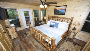 Une chambre dans une cabane en bois, avec un lit, un ventilateur de plafond, une table de chevet, une chaise et une fenêtre.