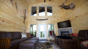 L’intérieur d’une cabane en rondins, avec une cheminée, des meubles en cuir et une tête de cerf accrochée au mur.