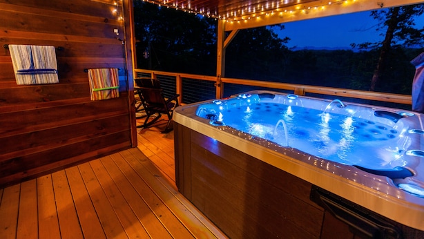 Une terrasse en bois avec un jacuzzi, des guirlandes lumineuses et une vue sur l’extérieur.