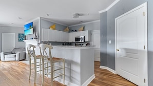 Una cocina moderna con armarios blancos, una isla central y una zona de comedor con dos sillas.