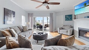 Una sala de estar con ventilador de techo, chimenea y un ventanal con cortinas.