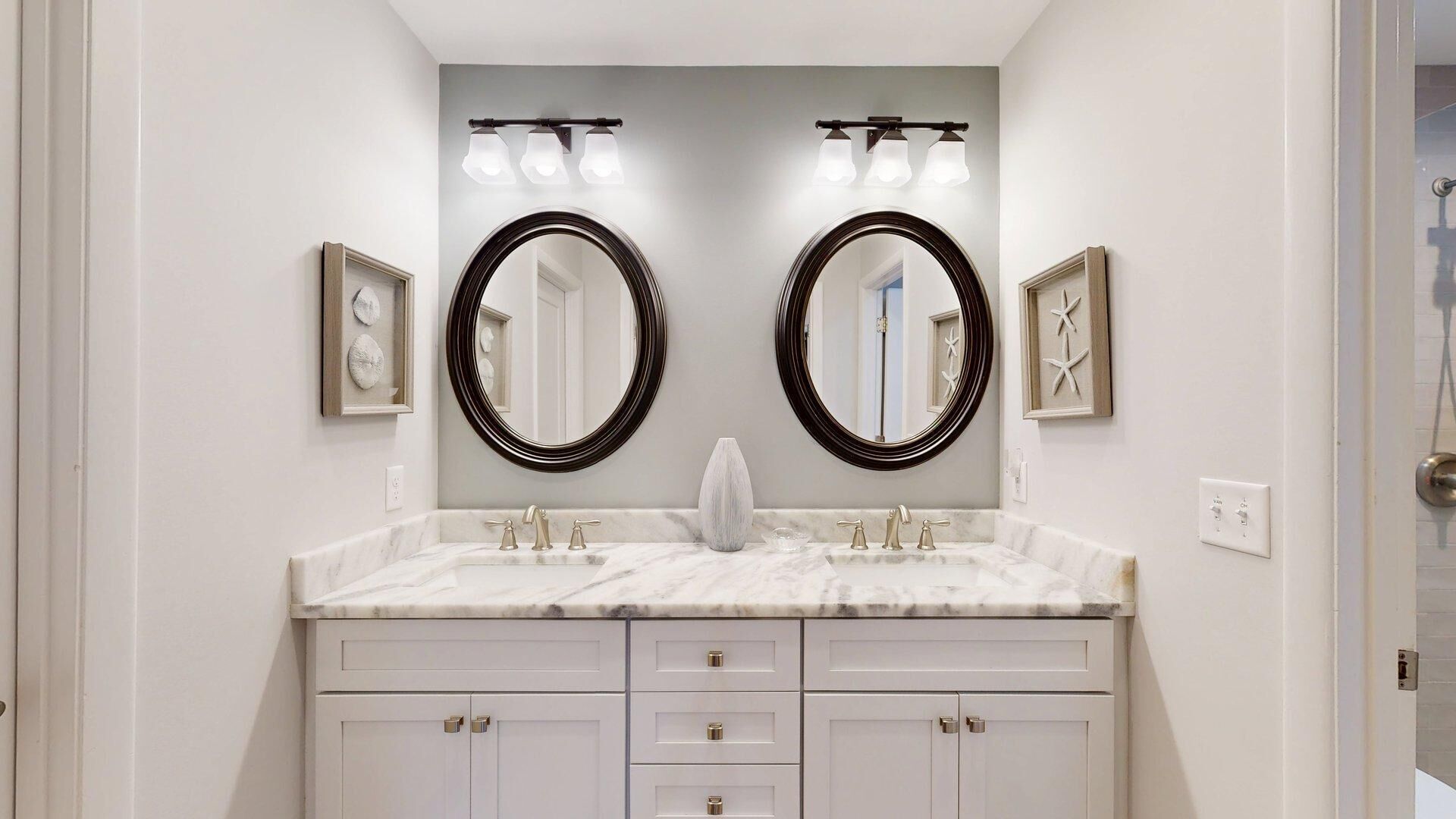 Une salle de bain dotée d’un meuble-lavabo double, de deux grands miroirs et d’un espace coiffeuse éclairé.