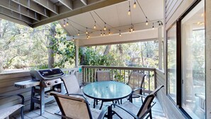 Une terrasse extérieure avec une table ronde et des chaises, un barbecue et des guirlandes lumineuses.