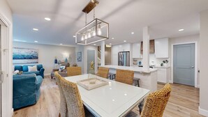 Un salon moderne avec une grande table blanche, des canapés bleus et des fauteuils en osier.