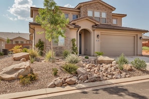 A two-story house with a stone facade, a garage, and a landscaped front yard with rocks and shrubs.
