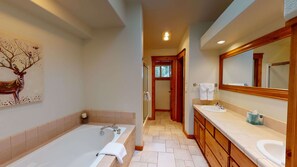 A modern bathroom with a large bathtub, a vanity with a mirror, and a wooden cabinet. - Group Getaway with Access to Exclusive Golf (Sunriver)