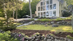 A house with a stone retaining wall, a small stream, and a driveway. - Beautiful lakefront home on Phillips Lake - Near Acadia! (Dedham)