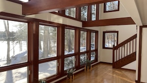 A spacious room with large windows, wooden beams, and a staircase. - Beautiful lakefront home on Phillips Lake - Near Acadia! (Dedham)