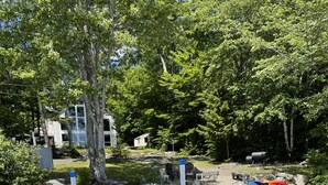 A wooden dock leading into a body of water, surrounded by trees and a small building in the background. - Beautiful lakefront home on Phillips Lake - Near Acadia! (Dedham)