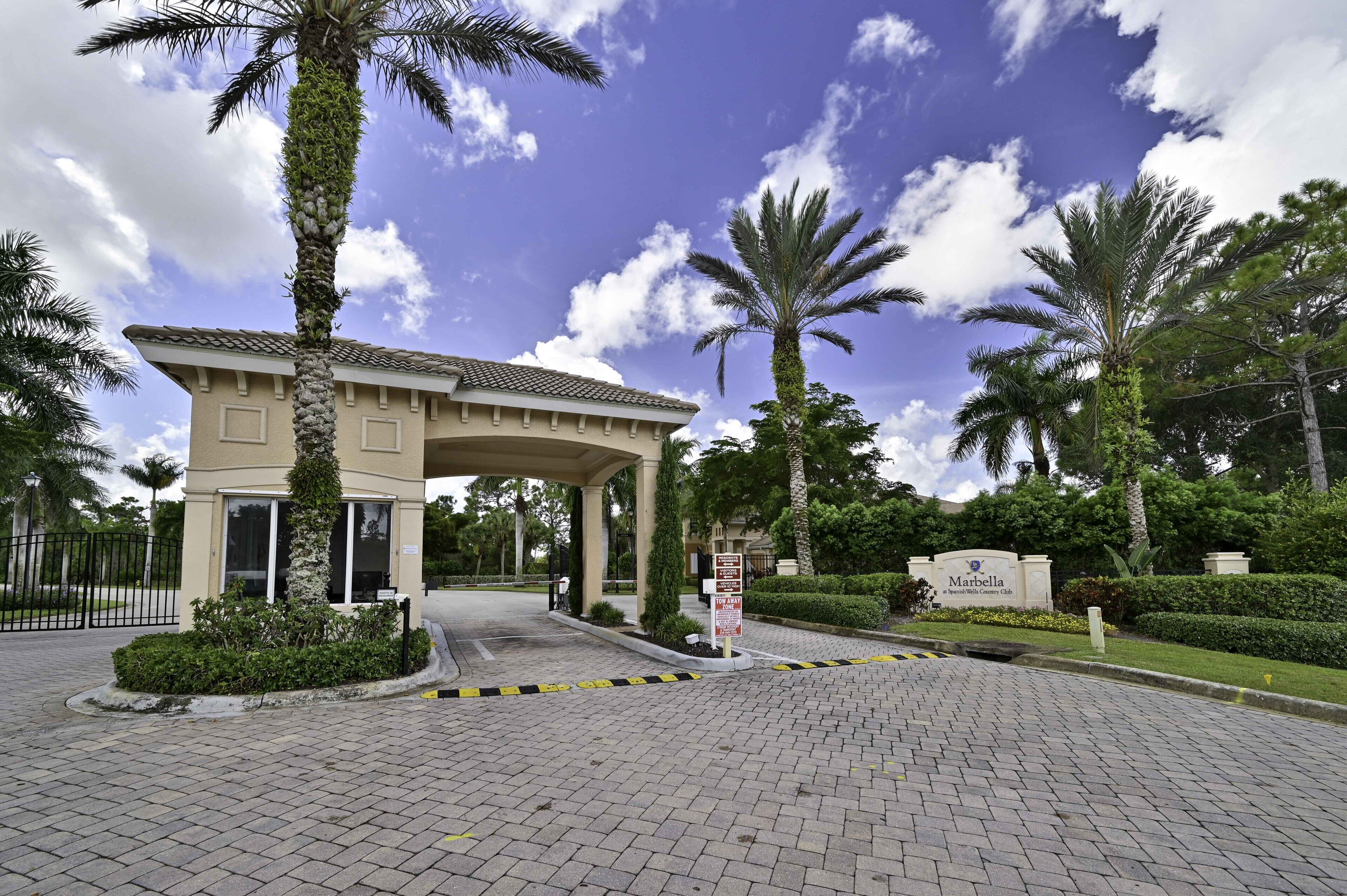A gated entrance to a property with a covered walkway, palm trees, and a sign indicating a 'Tow Away Zone.'